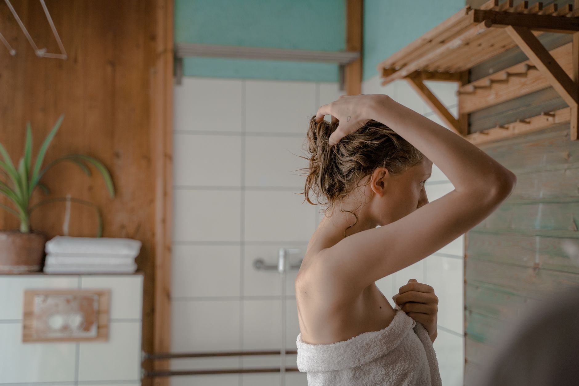 Woman in towel fixing hair in a warm, naturally lit bathroom, capturing serene and intimate moment.